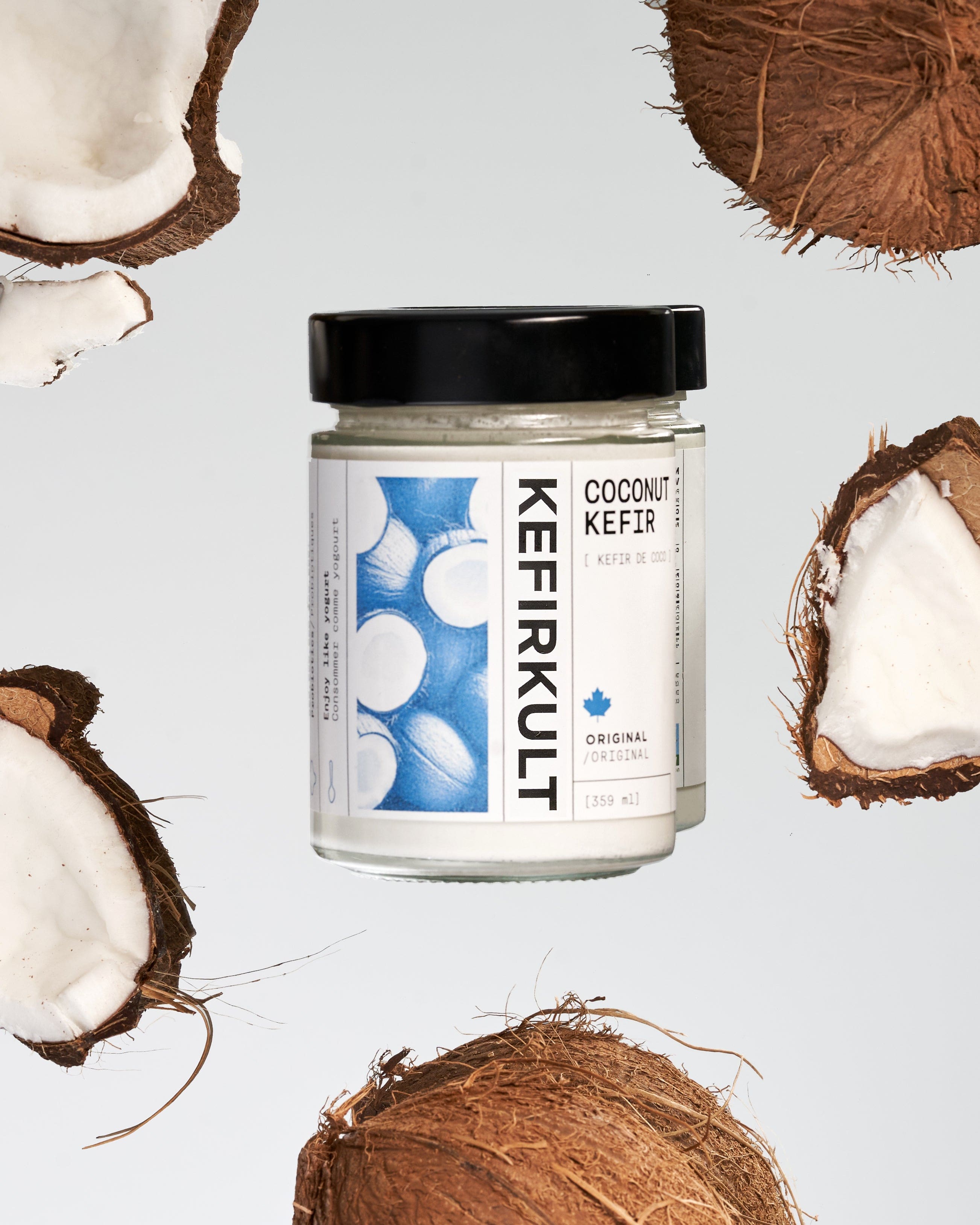 Jar of Kefirkult coconut kefir with a black lid on a white background, surrounded by halved coconuts.